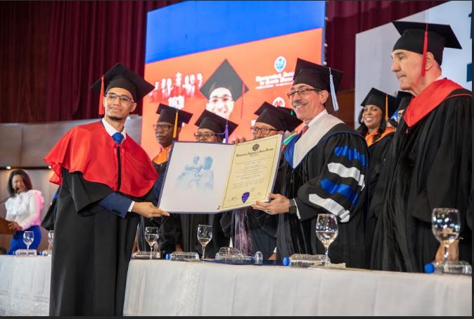 El rector de la UASD, doctor Jorge Asjana David entrega el título al graduado de mayor índice académico, Estarlin Rivas Báez (95.5 de promedio) de la licenciatura en Derecho de la Facultad de Ciencias Jurídicas y Políticas de la UASD.